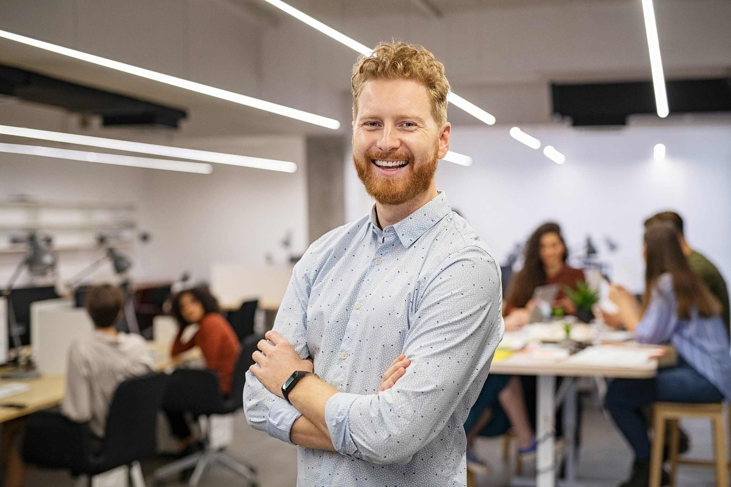 Smiling man in a collared shirt, standing in front of coworkers in an office setting
